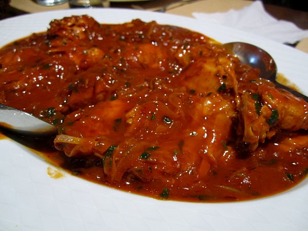 A closeup of a platter of braised meat in a bright red tomato sauce with herbs