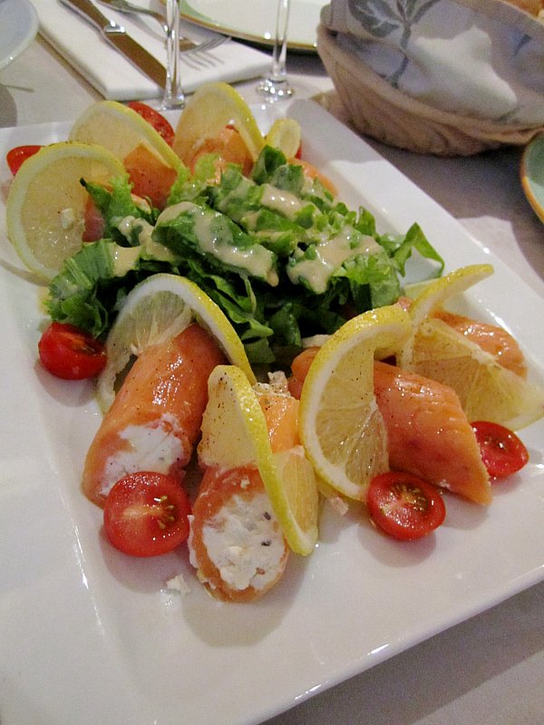 a plate of smoked salmon rolls filled with goat cheese and served with salad and lemons