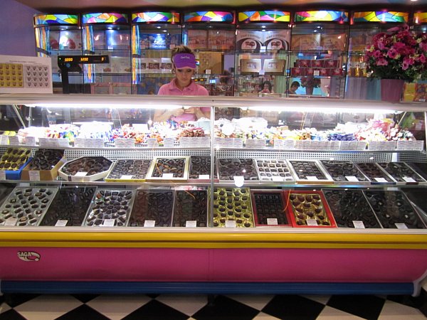 A chocolate display in a store with a woman standing behind the counter