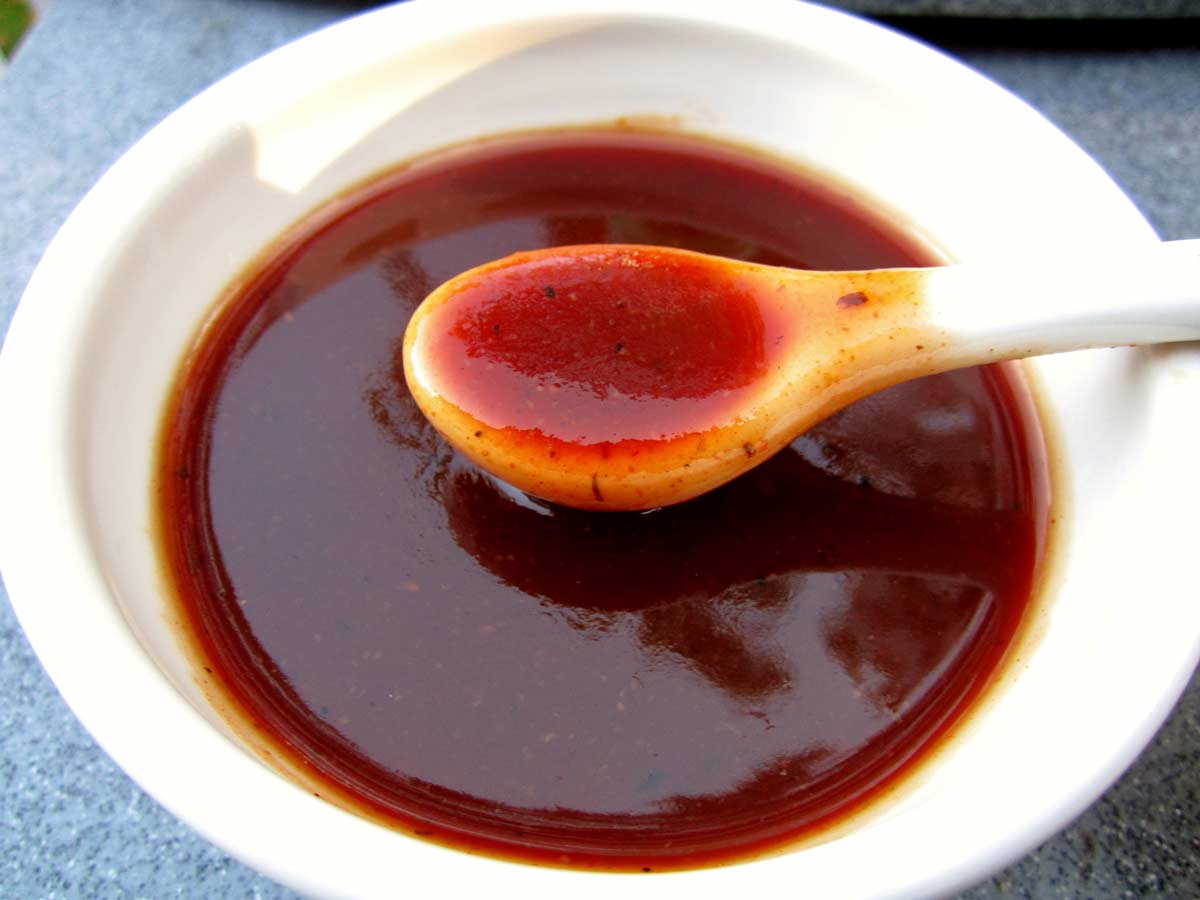 Homemade bbq sauce in a small white bowl with a white spoon lifting some out.