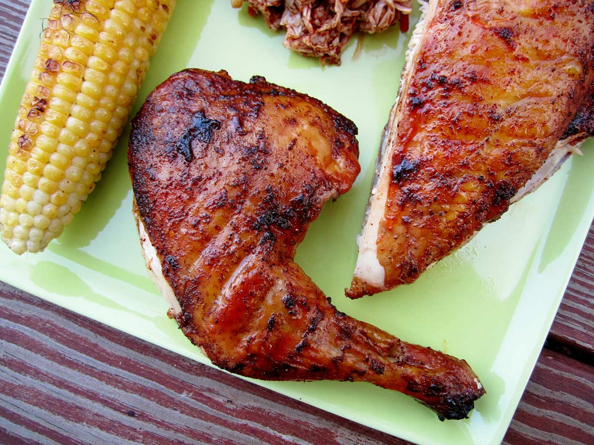 Smoked bbq chicken on a green plate with a side of slaw and grilled corn.