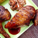 Closeup of smoked bbq chicken on a green plate with slaw and grilled corn.