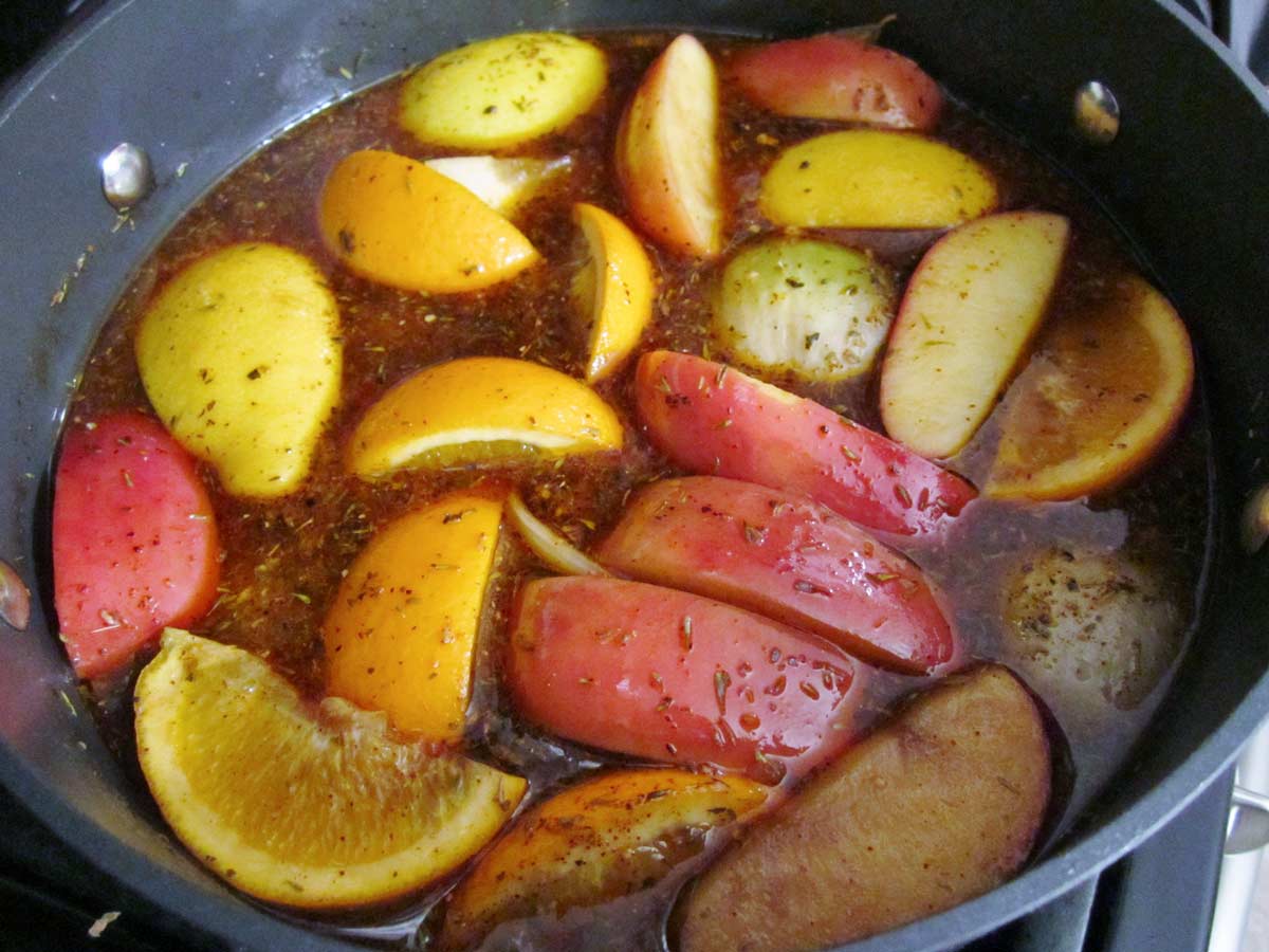 A pot of brine filled with pieces of apple, orange, and lemon.