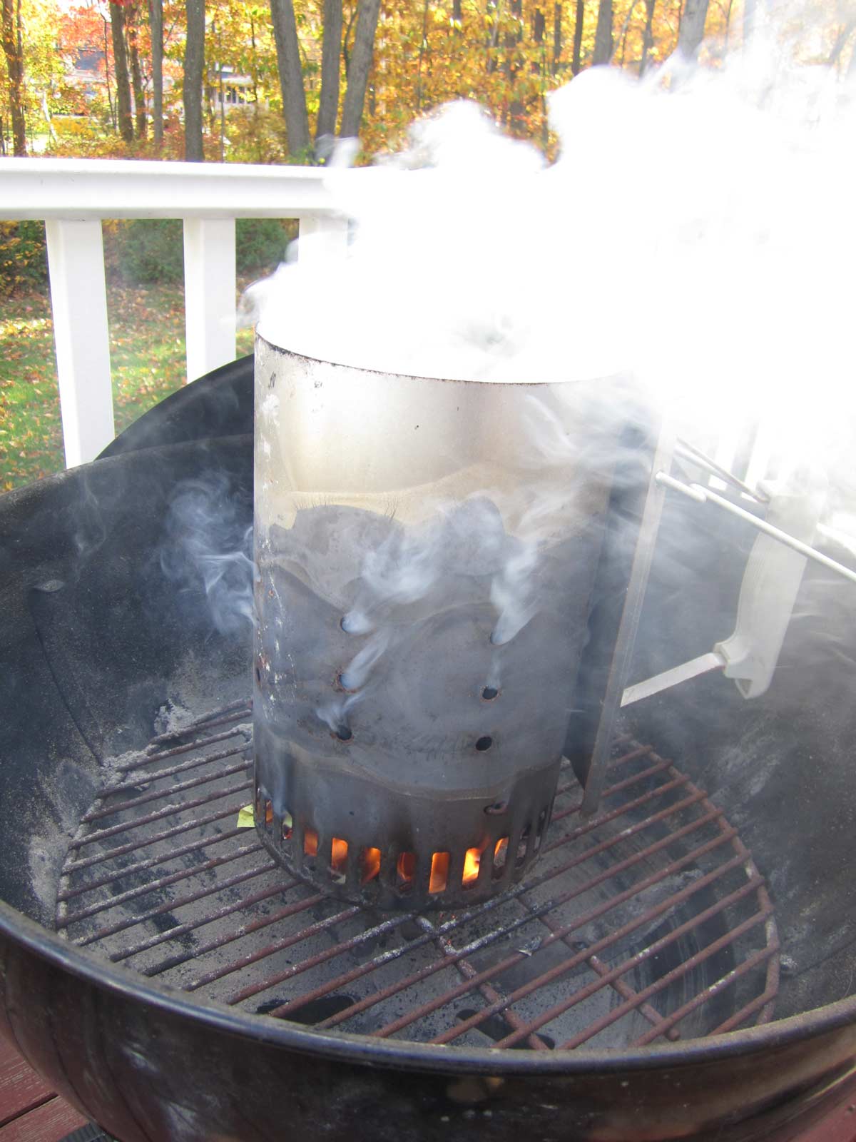 A chimney starter on a charcoal grill with smoke coming out of it.
