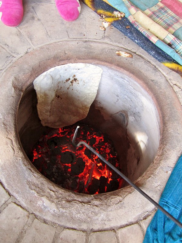 view looking down into a tonir underground oven with lavash bread baking inside