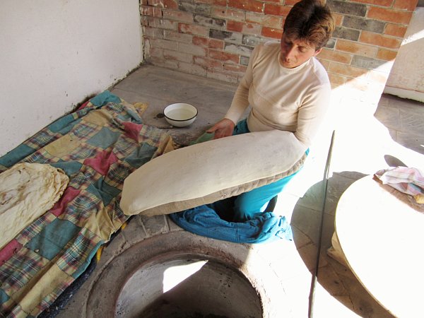 a woman sitting on the ground stretching a piece of dough over a large pillow