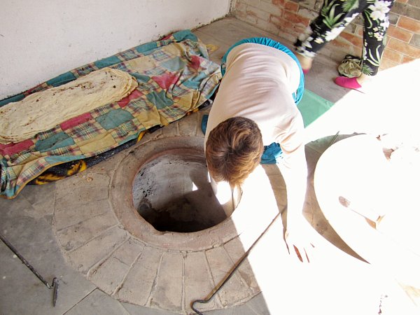 a woman sitting on the ground lowering something by hand into a hole