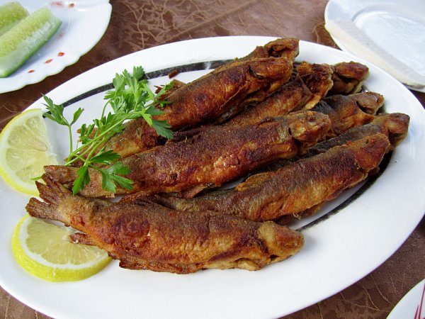 fried fishes on a white platter on a brown table