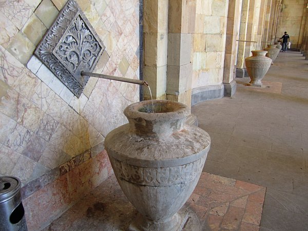 A large stone jug being filled with water from a faucet