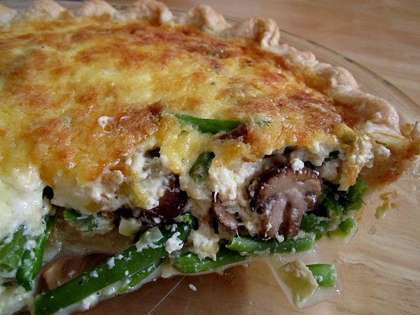 a closeup of a half eaten green bean and mushroom quiche in a glass pie dish