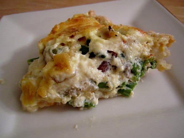 side view of a slice of green bean and mushroom quiche on a white plate