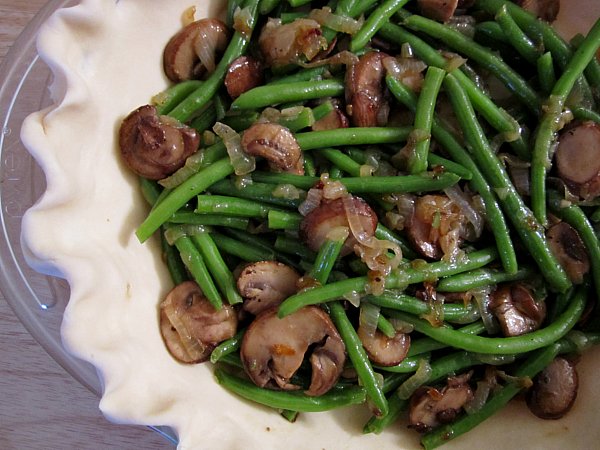 an unbaked pie crust filled with mushrooms and green beans