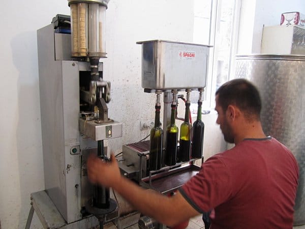 A man standing in front of a machine filling bottles with wine