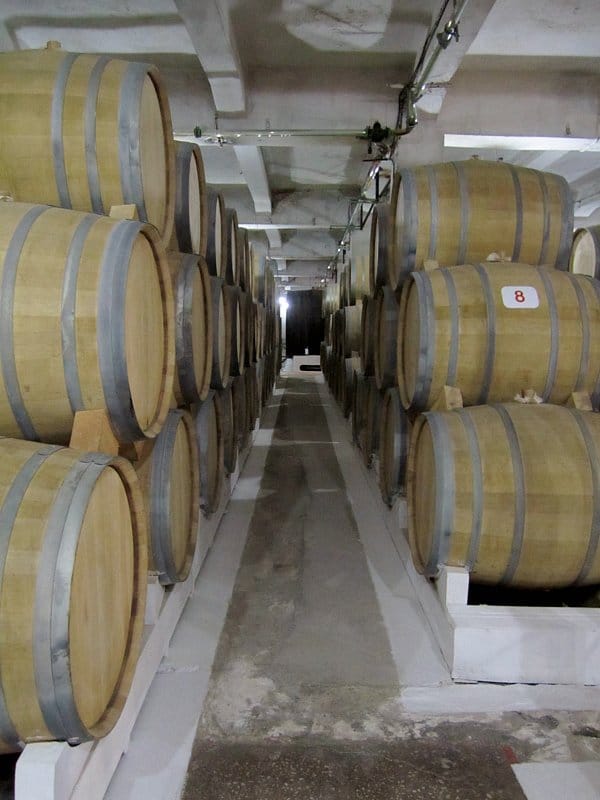 rows of wooden barrels piled high on either side of a narrow walkway
