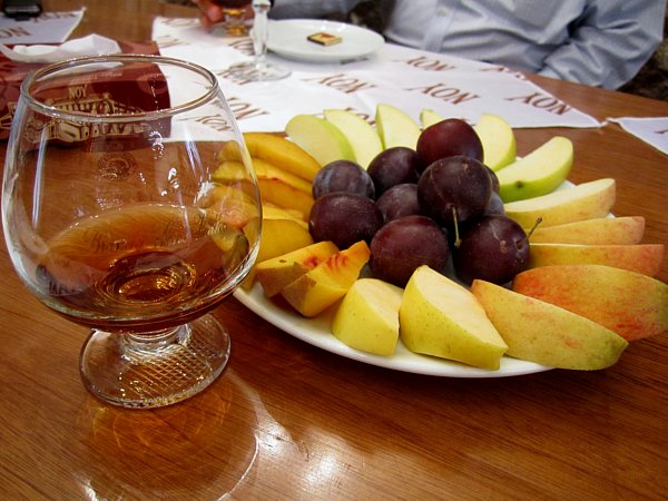 a platter of fruits next to a glass of brandy