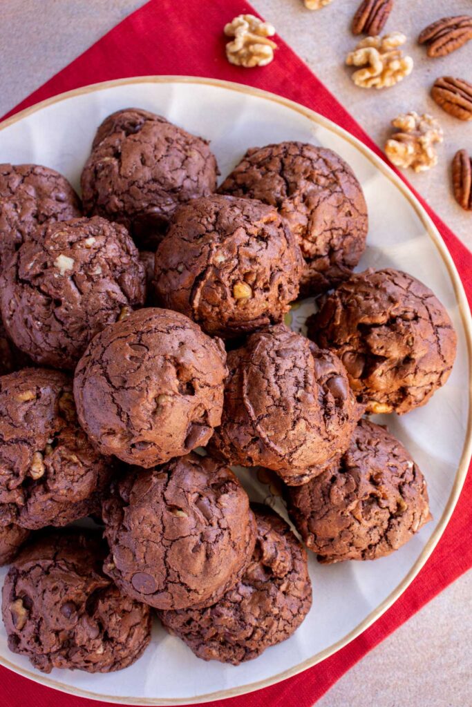 A plate of chocolate cookies on a red napkin with pecans and walnuts next to it.