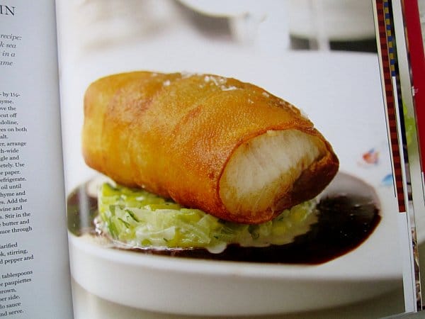 a piece of white fish wrapped in crispy fried potato served over leeks and brown sauce