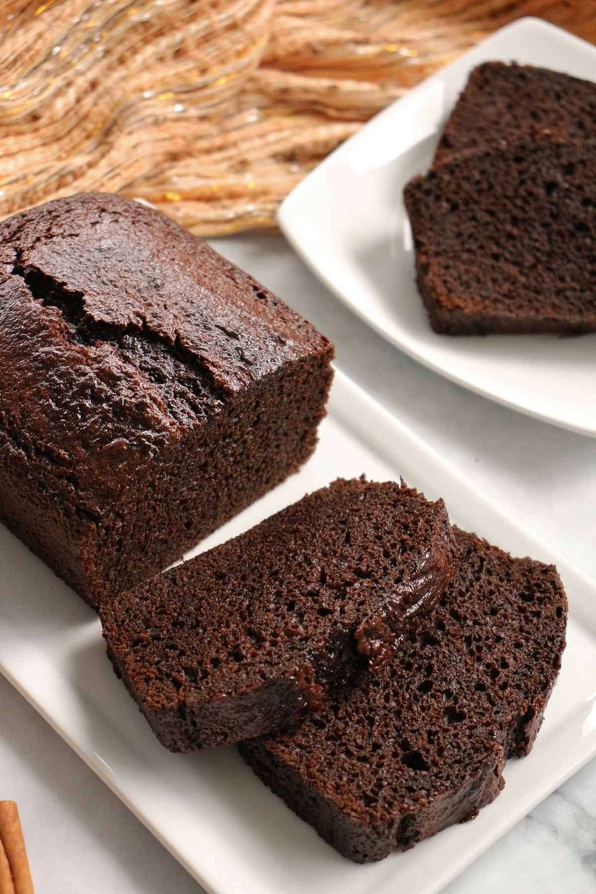 A partially sliced loaf of dark brown gingerbread on a white platter.