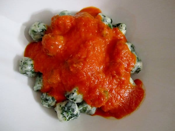 overhead view of spinach and ricotta gnudi dumplings on a white plate topped with tomato sauce