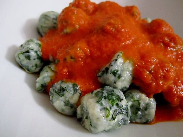 A closeup of spinach and ricotta dumplings topped with tomato sauce on a white plate