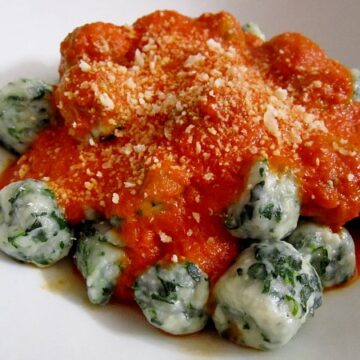 side view of a white plate topped with spinach and ricotto gnudi dumplings with tomato sauce