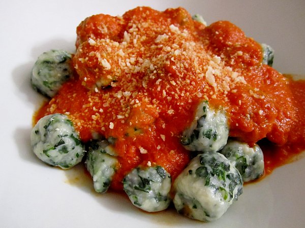 side view of a white plate topped with spinach and ricotto gnudi dumplings with tomato sauce