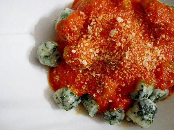spinach dumplings on a white plate topped with tomato sauce