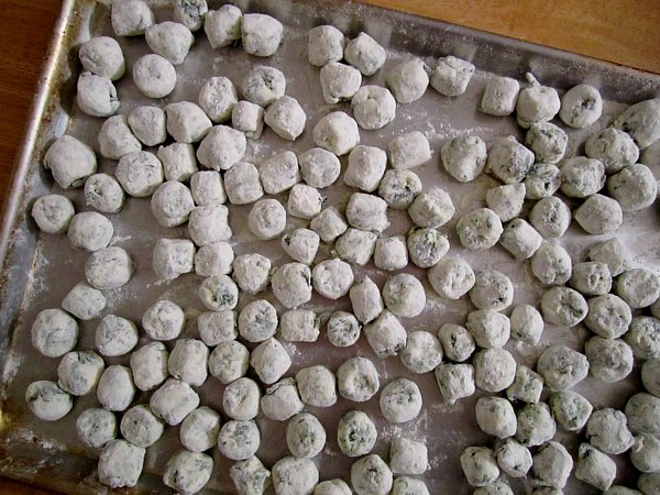 overhead view of small dumplings tossed in flour on a metal baking sheet