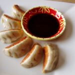 pan-fried dumplings fanned out around a red and yellow bowl of dipping sauce
