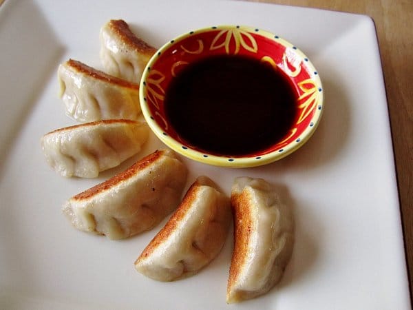 pan-fried dumplings fanned out around a red and yellow bowl of dipping sauce