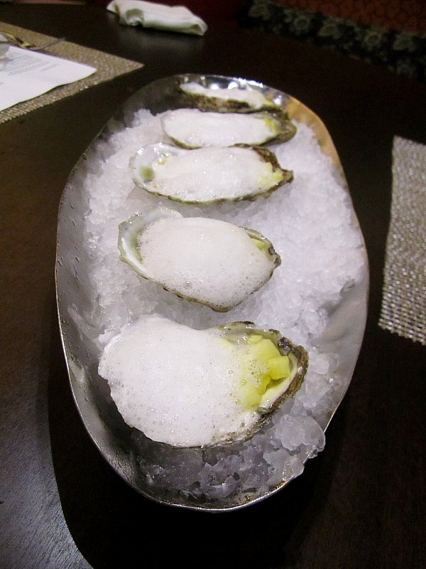 oysters on the half shell topped with white foam served over crushed ice