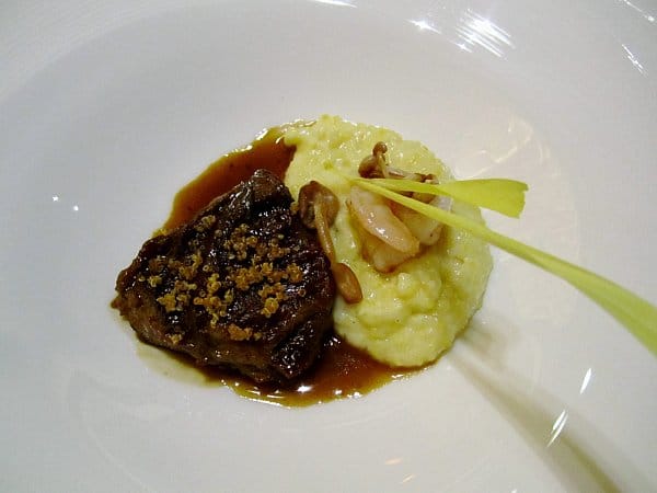 braised meat served with a creamy corn puree and mushrooms on a white dish