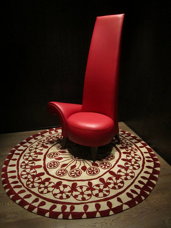 a very tall red chair on a round red and white rug