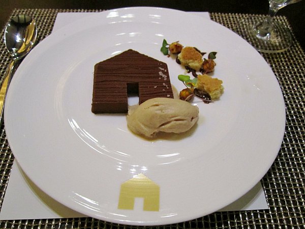 a chocolate house shaped dessert with ice cream on a white plate