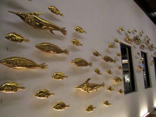 a white wall covered with gold fish figures with hands as tails