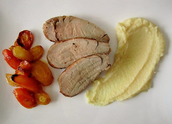 three slices of roasted pork tenderloin with carrots and white puree on a white plate