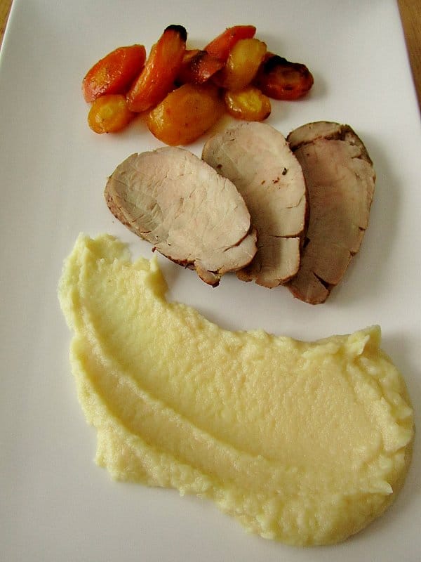 a white rectangular plate with roasted pork tenderloin slices, carrots, and parsnip puree