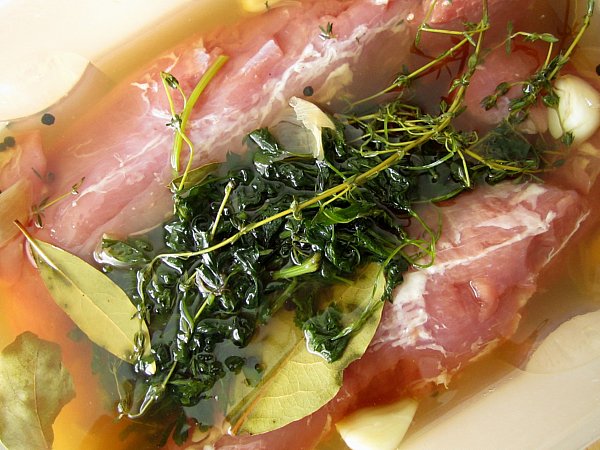 two pork tenderloins in brine with a pile of herbs on top