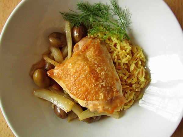 overhead view of a crispy chicken thigh with olives and rice in a white dish