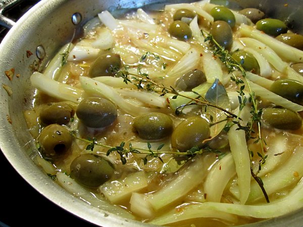 a pan of fennel, green olives, and herbs cooking together in some liquid