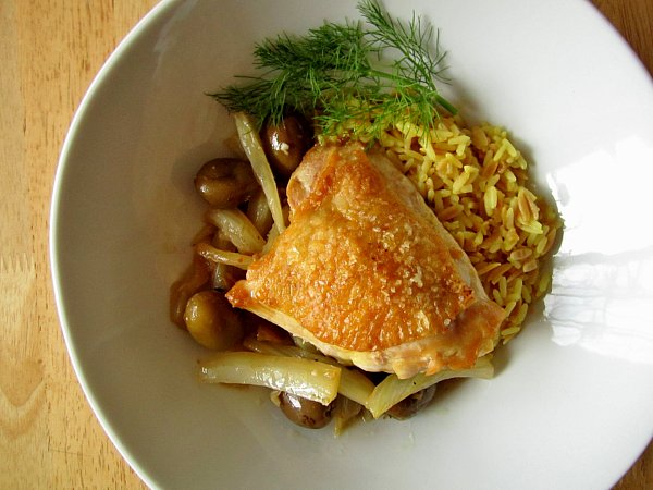 wide view of a chicken thigh with olives, fennel and rice in a round white dish