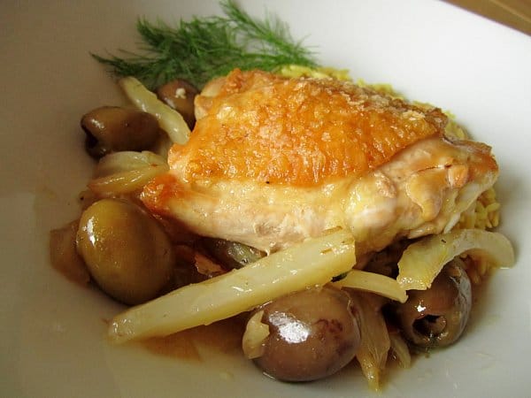 closeup of cooked strips of fennel and green olives topped with a crispy chicken thigh