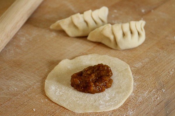 a round piece of dough on a wooden board topped with a scoop of brown filling