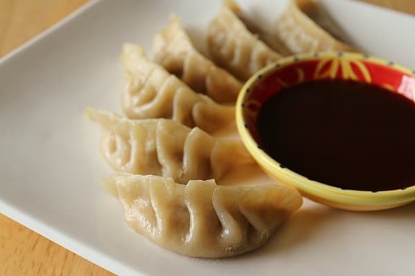 A closeup of Asian dumplings on a white plate next to a bowl of sauce