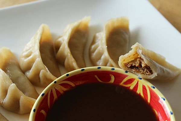 dumplings arranged on a white plate around a yellow and red bowl of dipping sauce