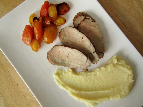overhead view of a rectangular white plate with roasted carrots, sliced pork tenderloin, and parsnip puree