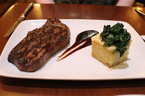 a cooked steak on a white plate next to a square shaped potato gratin