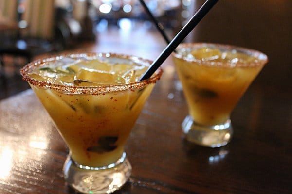 two cocktails in glasses with black straws on a wooden table