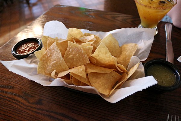 a basket of tortilla chips with cups of red and green salsa on either side