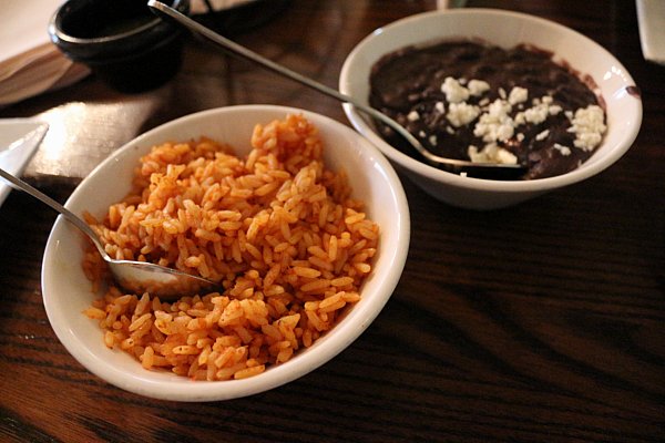 bowls of red rice and black beans on a wooden table